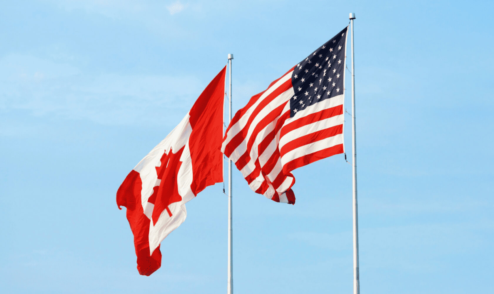 Un drapeau canadien et un drapeau americain flottent au vent.