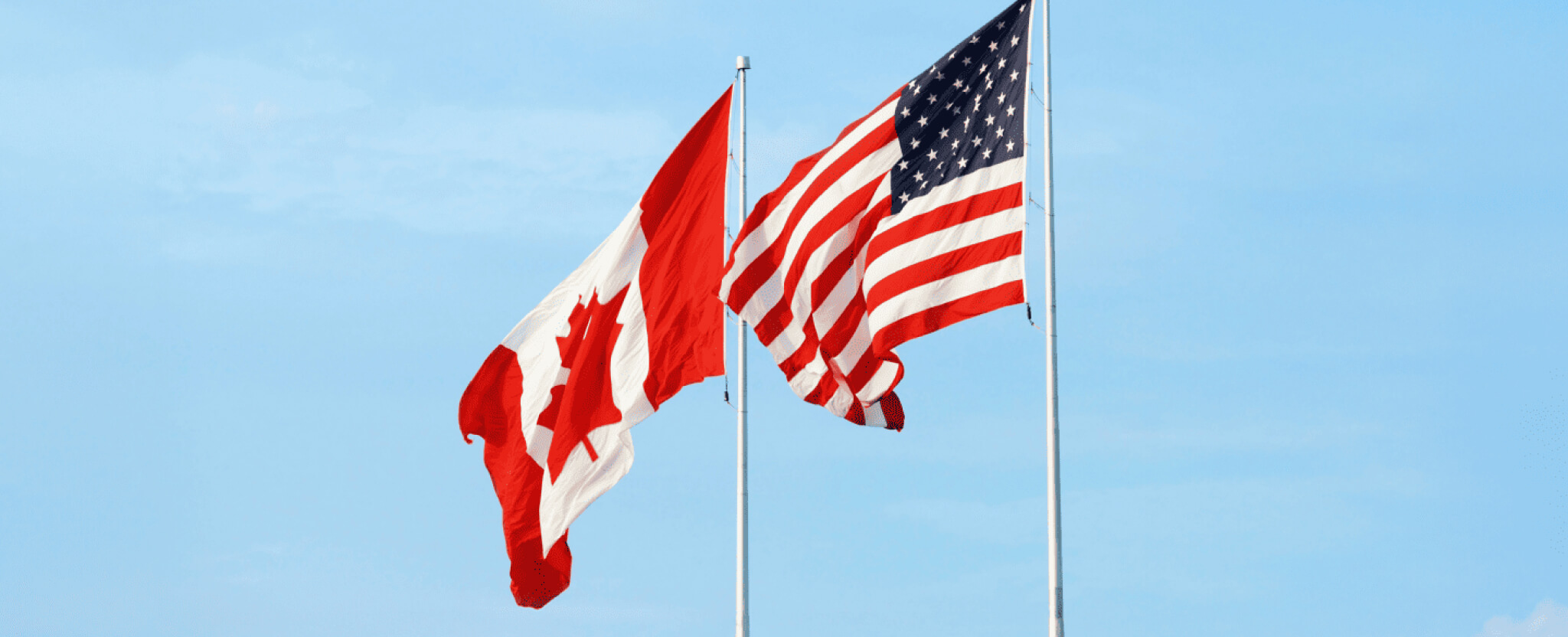 Un drapeau canadien et un drapeau americain flottent au vent.