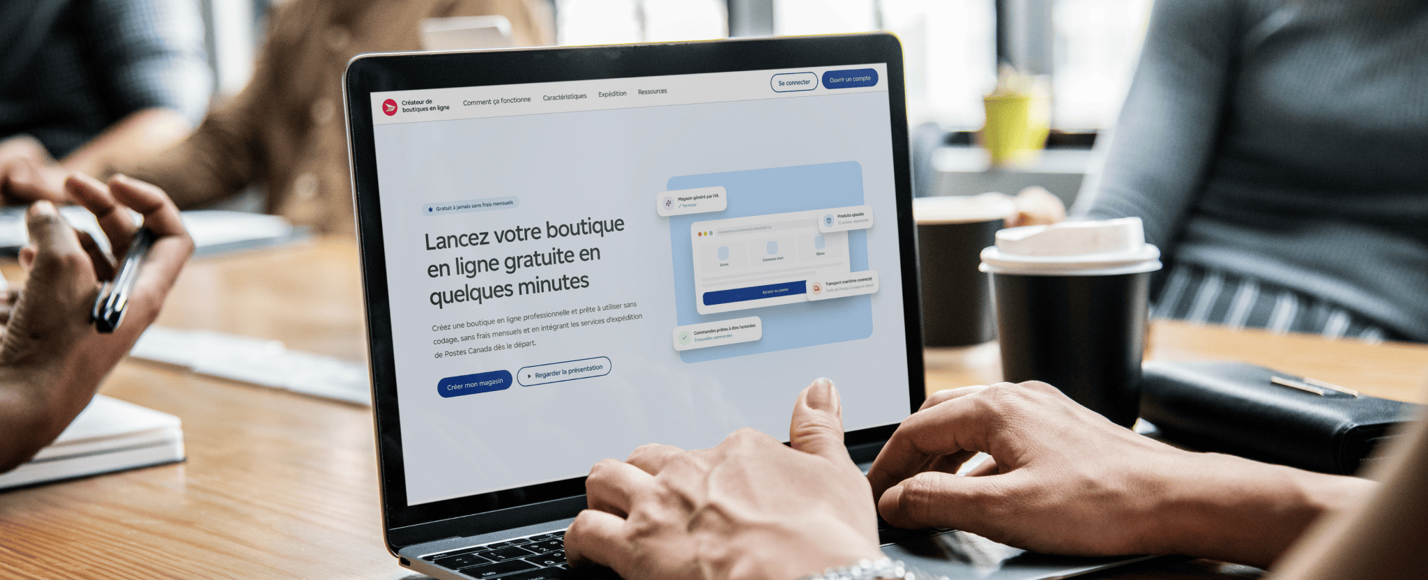 Les mains d’une personne sur le clavier d’un ordinateur portable affichant la page de l’outil de création de boutiques en ligne. Sur la table de travail, il y a un téléphone intelligent, une tasse à café et des articles de bureau.