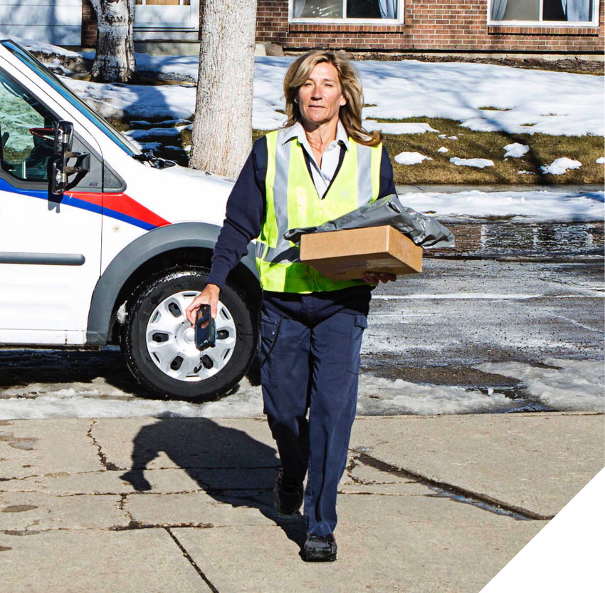 Travailleuse de Postes Canada marchant dans une rue glacée et transportant plusieurs paquets.