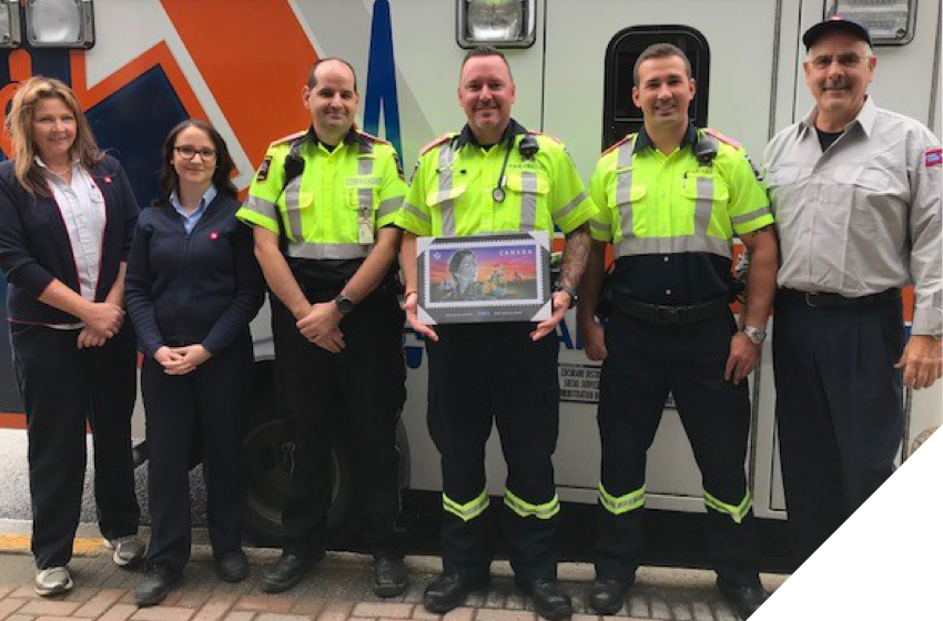 Employés de Postes Canada donnant une plaque du timbre sur les intervenants d’urgence à des paramédics à Timmins (Ont.).