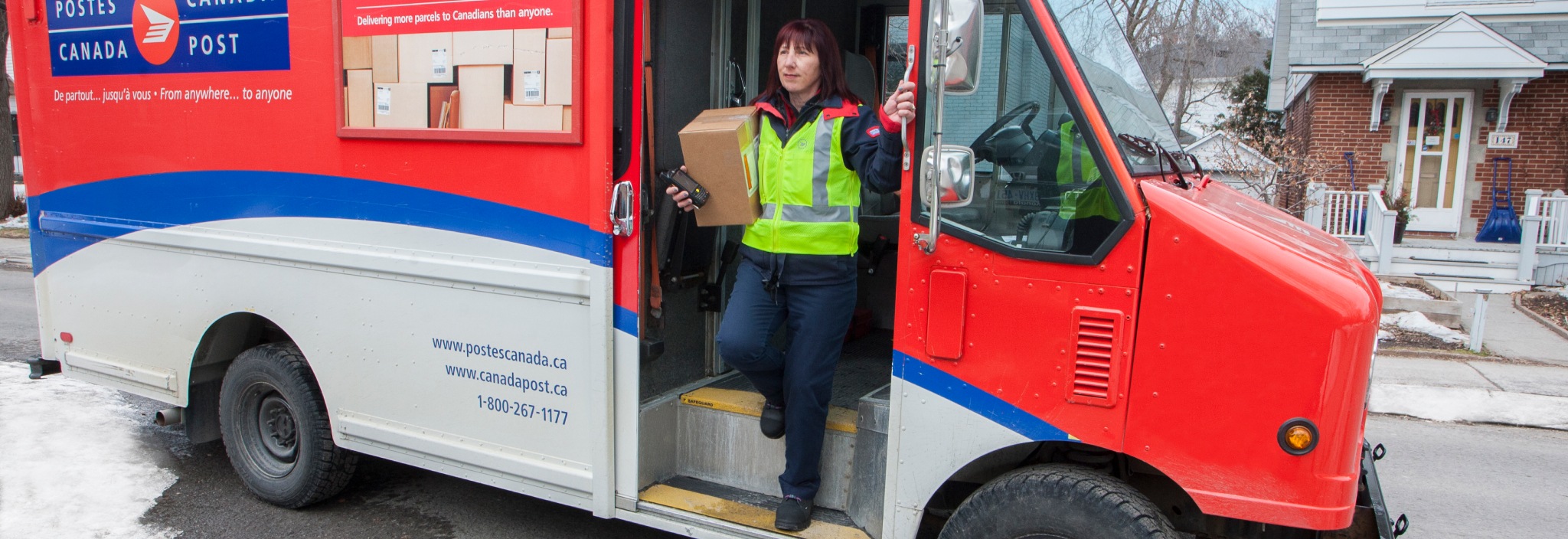 Agente de livraison sortant d’un camion de Postes Canada dansun quartier résidentiel pour livrer un colis