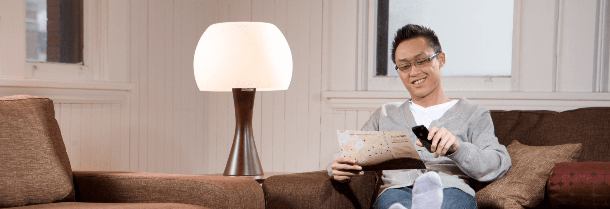 Un jeune homme assis sur un canapé dans un salon lit un dépliant.