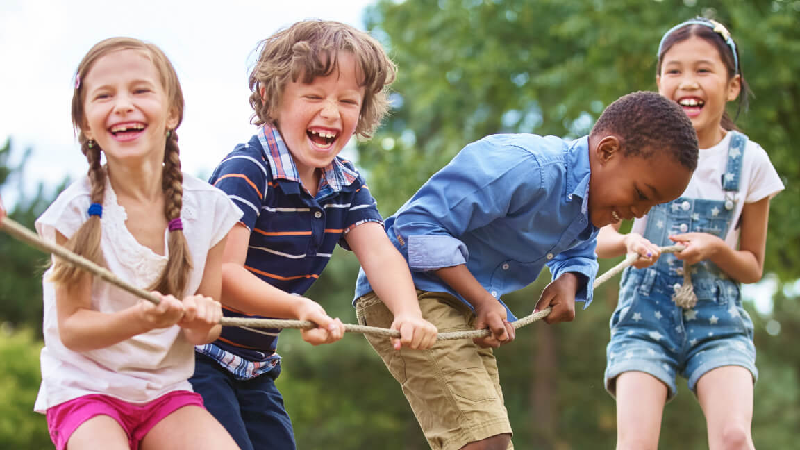 Quatre enfants rient en faisant du tir à la corde dans un parc.