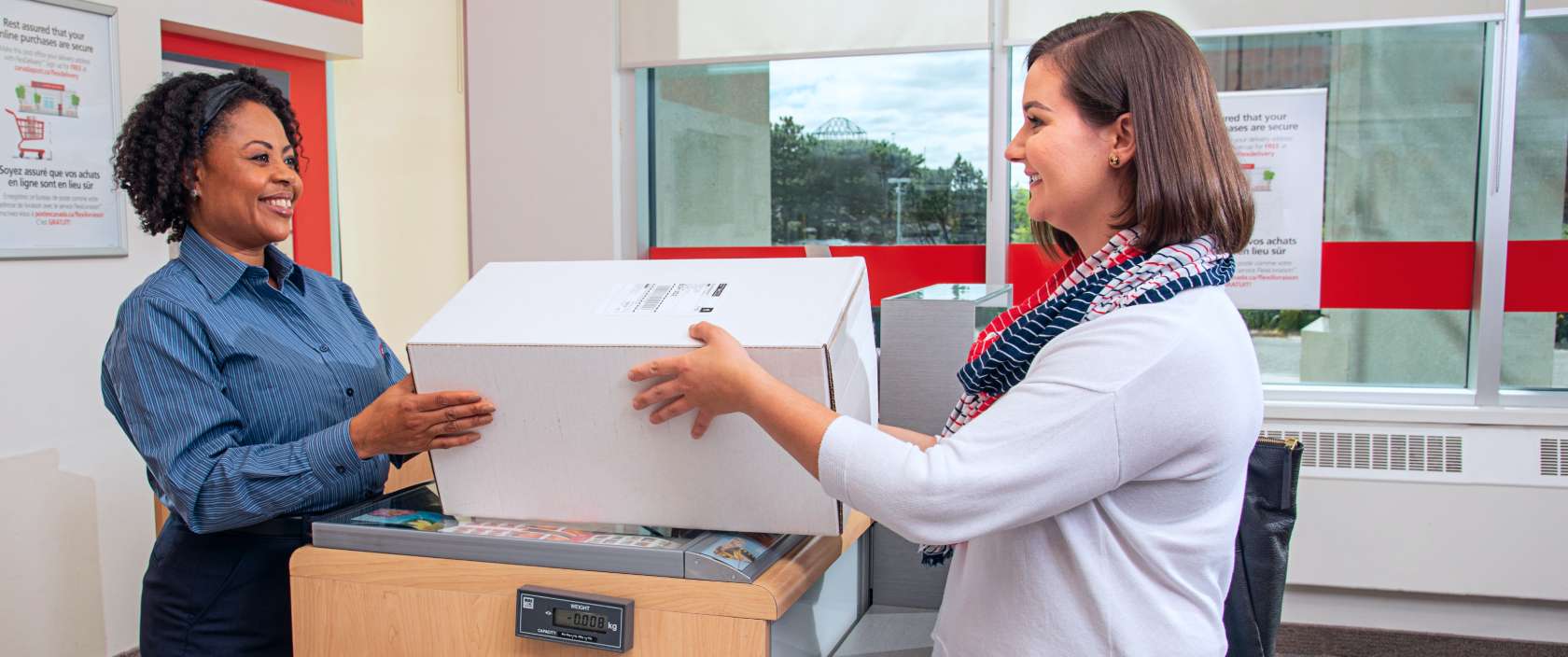 Une commis remet un colis à une femme qui ramasse son achat effectué en ligne à son comptoir postal local de Postes Canada