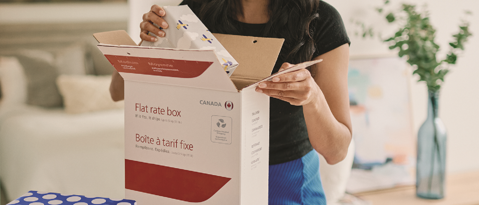 Une femme achète une boîte à tarif fixe de Postes Canada à un comptoir de bureau de poste