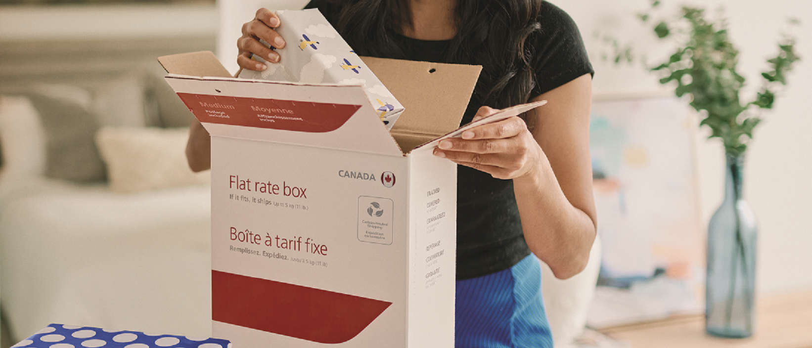 Une femme place un cadeau emballé dans une boîte à tarif fixe de Postes Canada.