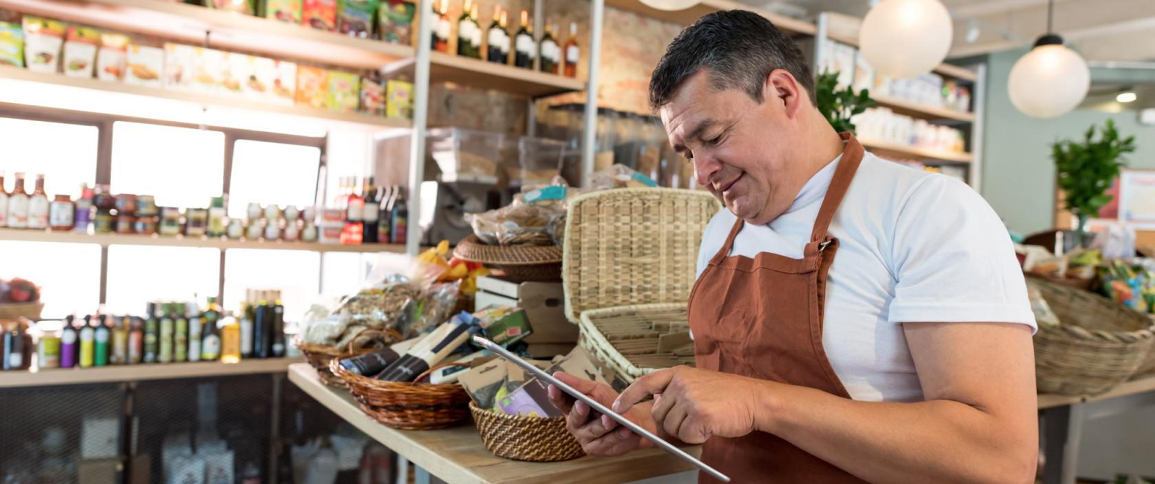 Un homme en tablier utilise une tablette dans une épicerie gourmande.