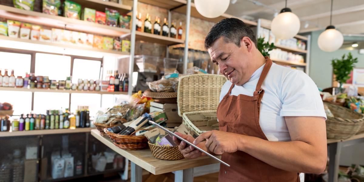 Un homme en tablier utilise une tablette dans une épicerie gourmande.