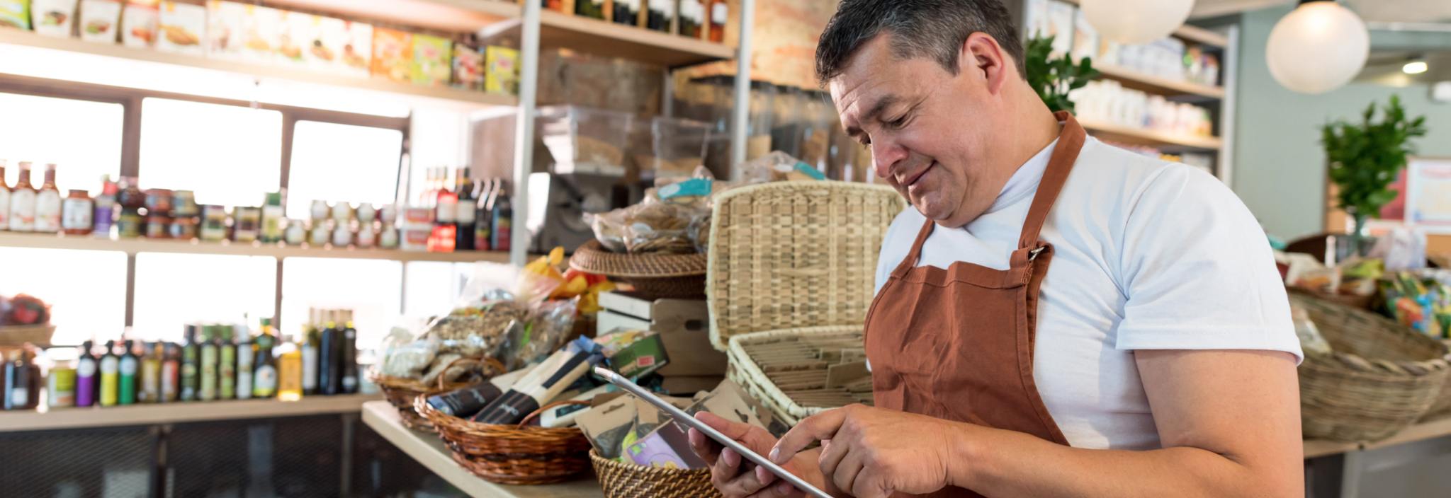Un homme en tablier utilise une tablette dans une épicerie gourmande.