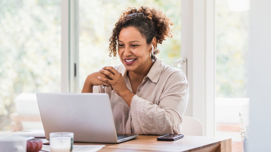 Une femme est assise devant un ordinateur portable et prend des notes manuscrites.